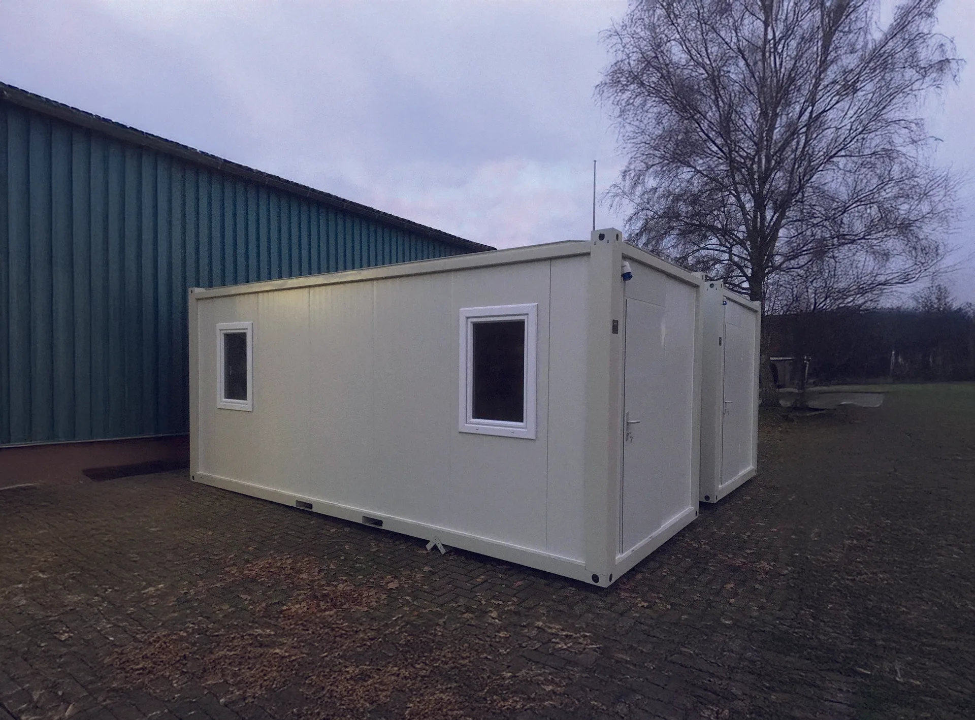 MODDOLIVING P2260 M flatpack container — exterior view of a pair of insulated cabins on a hardstand under overcast sky.